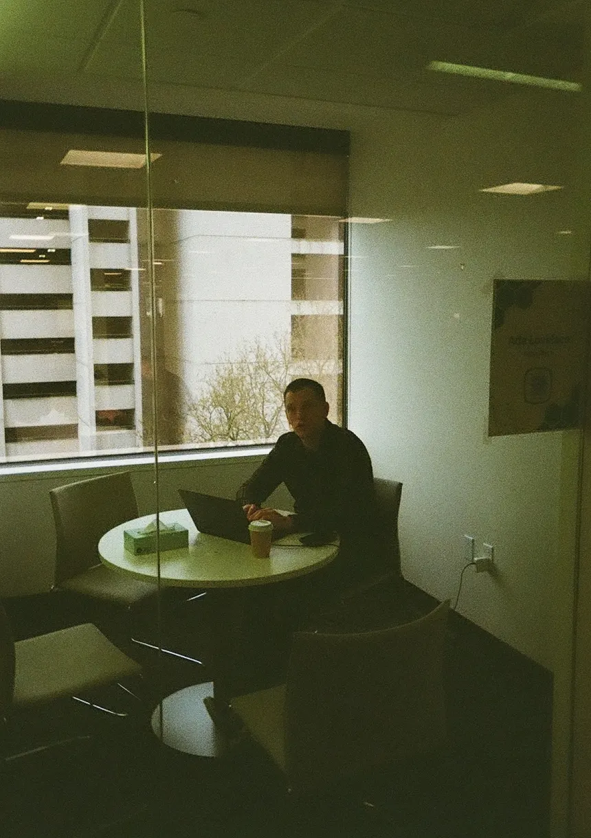 A teammate working alone at a laptop in a glass-walled meeting room.