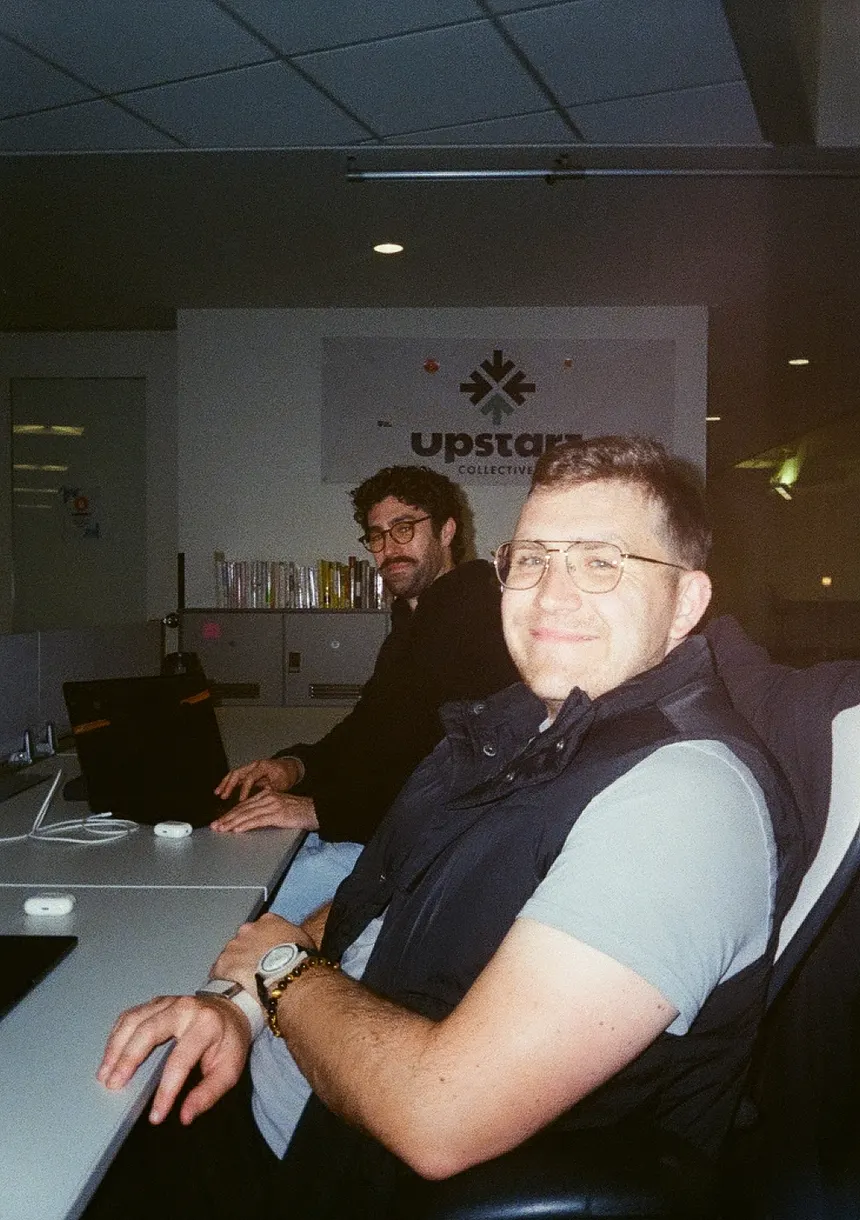 Two teammates at a shared desk, turning to the camera.